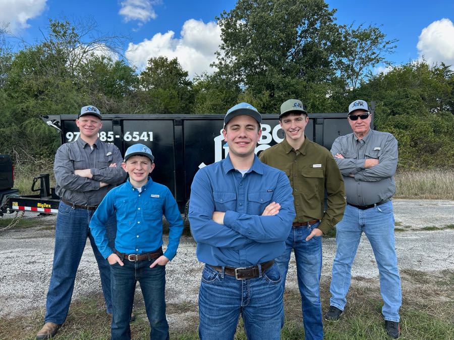 The BCS Junk Removal crew standing on a gravel lot in front of the black BCS Junk dump trailer